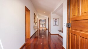 A hallway with wooden flooring, wooden doors, and a kitchen visible through an open door.