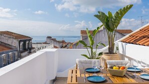 Terraza en la azotea con una mesa dispuesta para dos personas, con vistas a la ciudad y al mar.