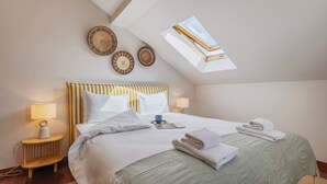 A bedroom with a sloped ceiling, a bed with white bedding, two bedside lamps, and a skylight.