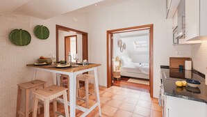 A modern kitchen with a dining area, wooden stools, and a view into a bedroom.