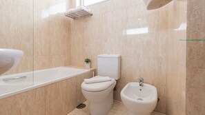 Un baño moderno con bañera, inodoro, bidé y una pequeña planta en maceta.