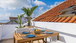 Una terraza en la azotea con una mesa para dos, plantas en macetas y vistas de la ciudad.