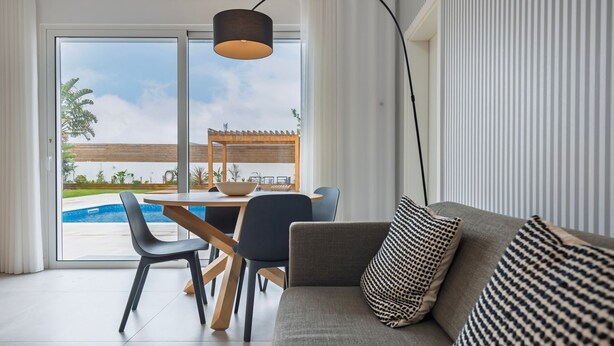 Ein modernes Wohnzimmer mit Blick auf einen Pool, einem Essbereich und einem Sofa mit gemusterten Kissen.