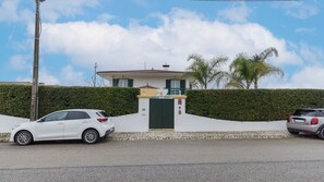 residence with a two-story house, green gate, and balcony, set amidst a well-maintained garden and paved driveway.