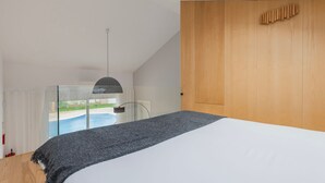 Ein modernes Schlafzimmer mit einem großen Bett, Blick auf einen Swimmingpool und einem Holzschrank.