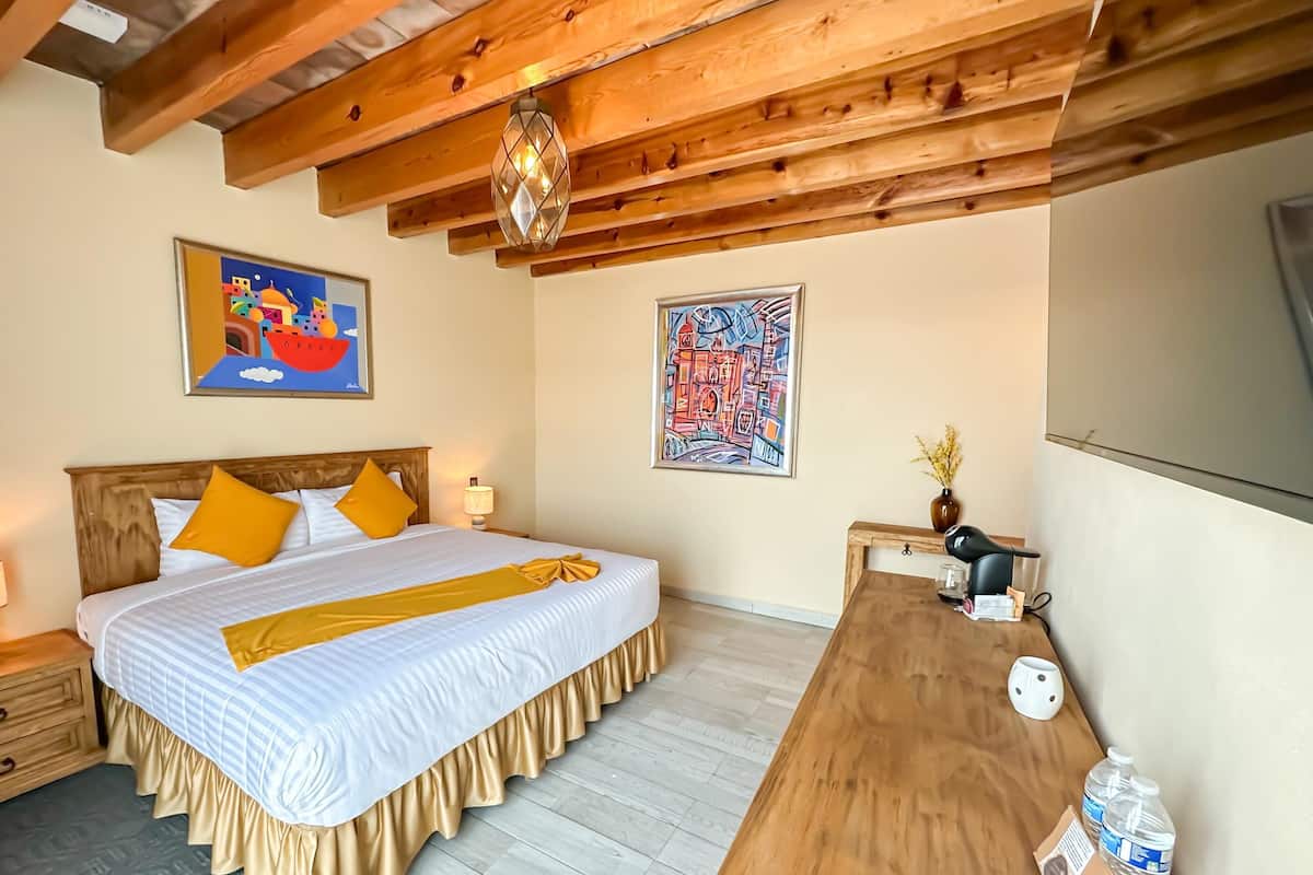 Ein Hotelzimmer mit Holzboden, einem Bett mit gelben Kissen, einem Holztisch mit Fön und zwei Wasserflaschen.