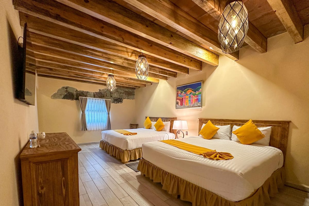 Ein Hotelzimmer mit zwei Betten, Holzboden, einer Steinwand, einem Gemälde und einem Holzkasten.