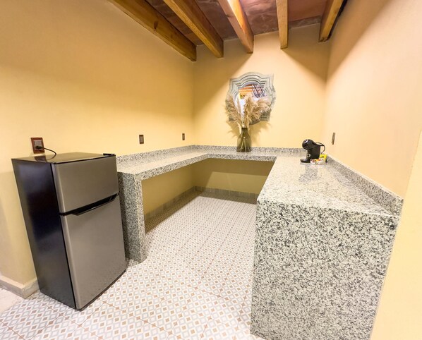 Una cocina con refrigerador, encimera de granito, piso estampado y un florero con plantas secas.