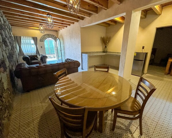 A cozy living room with a fireplace, a dining area with a round table and chairs, and a kitchen area with a refrigerator.
