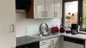 A modern kitchen with white cabinets, a dishwasher, an oven, a sink, and a window with a view of a house and trees.