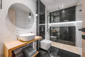 A modern bathroom with a round mirror, a white sink, a toilet, and a glass-enclosed shower area.