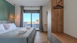 A modern hotel room with a large bed, grey curtains, a wooden bench, and a view of the city. - Rosy pair,private pool & jacuzzi near waterpark & Beach (Anopolis)