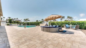 Un espace aménagé au bord de la piscine, avec des sièges disposés en cercle, un parasol en chaume et une piscine.