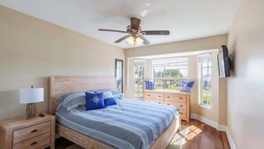 Une chambre à coucher comprenant un lit, une table de chevet, une commode et un ventilateur de plafond.