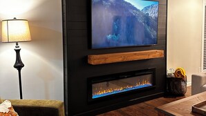 A living room with a flat-screen TV mounted on a wall, a fireplace below it, a sofa, a lamp, and a coffee table.
