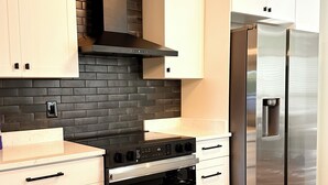 A modern kitchen with white cabinets, a black brick backsplash, stainless steel appliances, and wooden flooring.