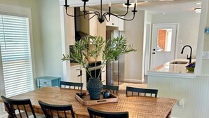A dining room with a wooden table, black chairs, a chandelier, and a potted plant.