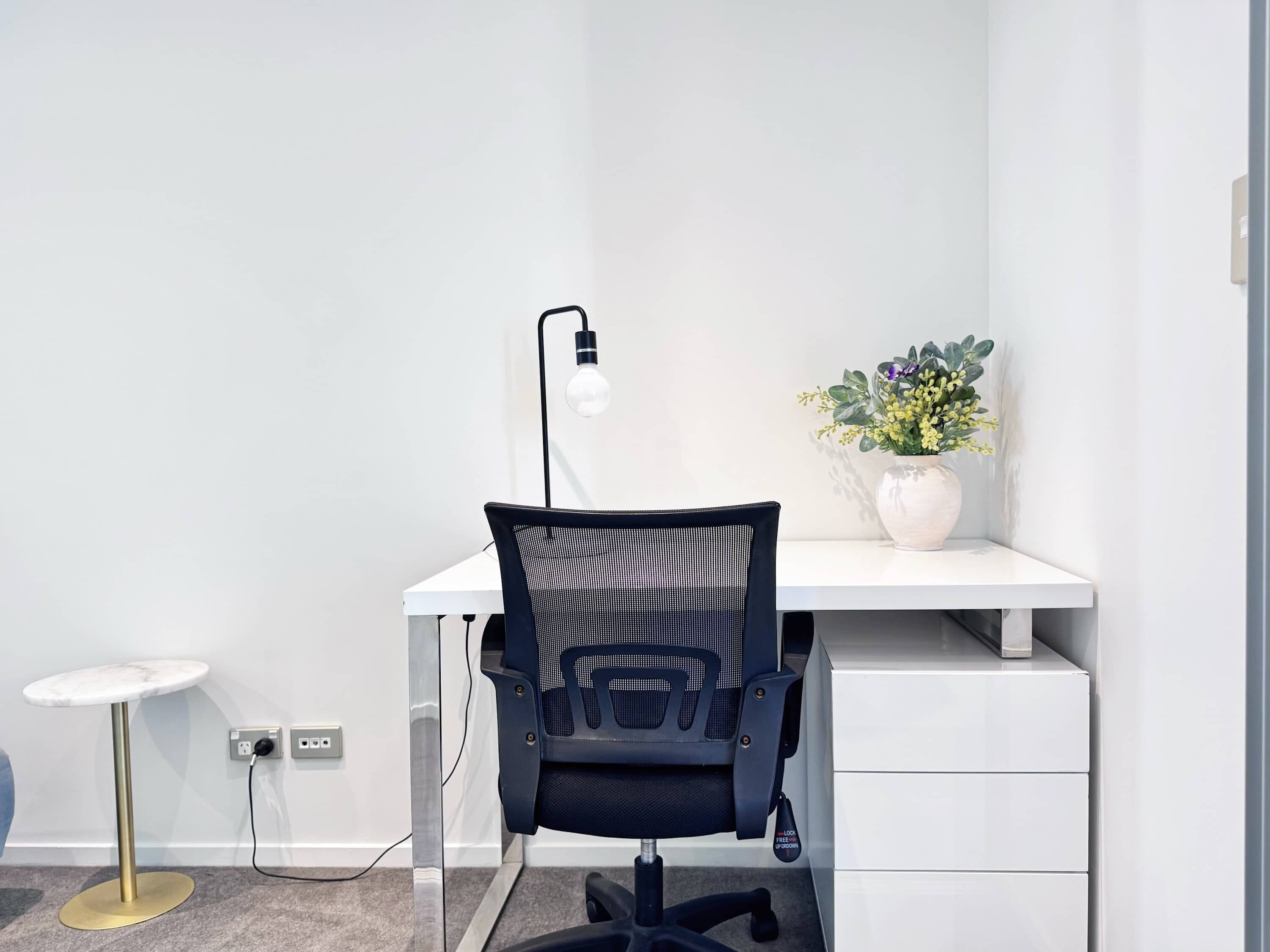 Ett modernt kontorsutrymme med ett skrivbord, en stol, en lampa och en liten krukväxt.