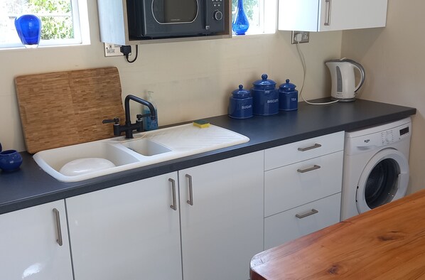 A kitchen with a sink, microwave, and washing machine. - Bali Hi Cliff Cottage-sleeps 2-hot Tub-5minbeach (Sheerness)