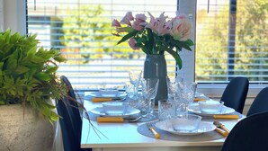 A dining table set with clear glassware, plates, and cutlery, with a vase of flowers in the center. - Bungalow Sint Maartenszee Near Sandy Beach (Sint Maartensvlotbrug)