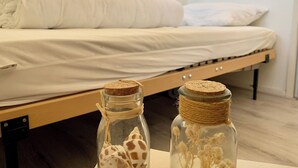 A single bed with a white mattress and pillows, a wooden frame, and a small table with two glass jars containing dried flowers. - Bungalow Sint Maartenszee Near Sandy Beach (Sint Maartensvlotbrug)