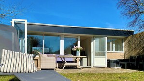 A modern house with a glass door leading to a patio area. - Bungalow Sint Maartenszee Near Sandy Beach (Sint Maartensvlotbrug)