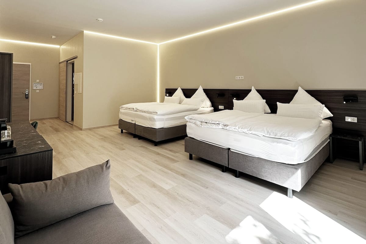 A modern hotel room with two beds, a sofa, and a TV.