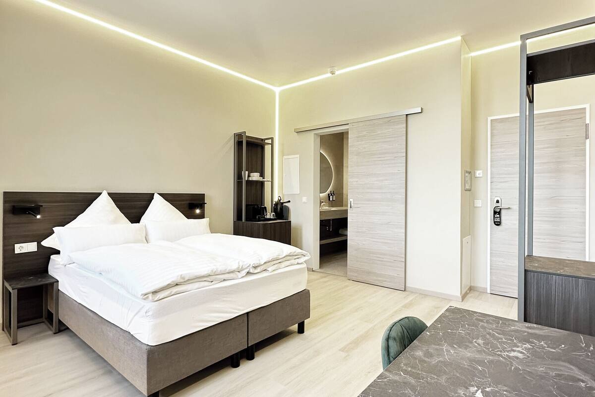 A modern hotel room with a bed, bedside tables, a desk, and a wardrobe.
