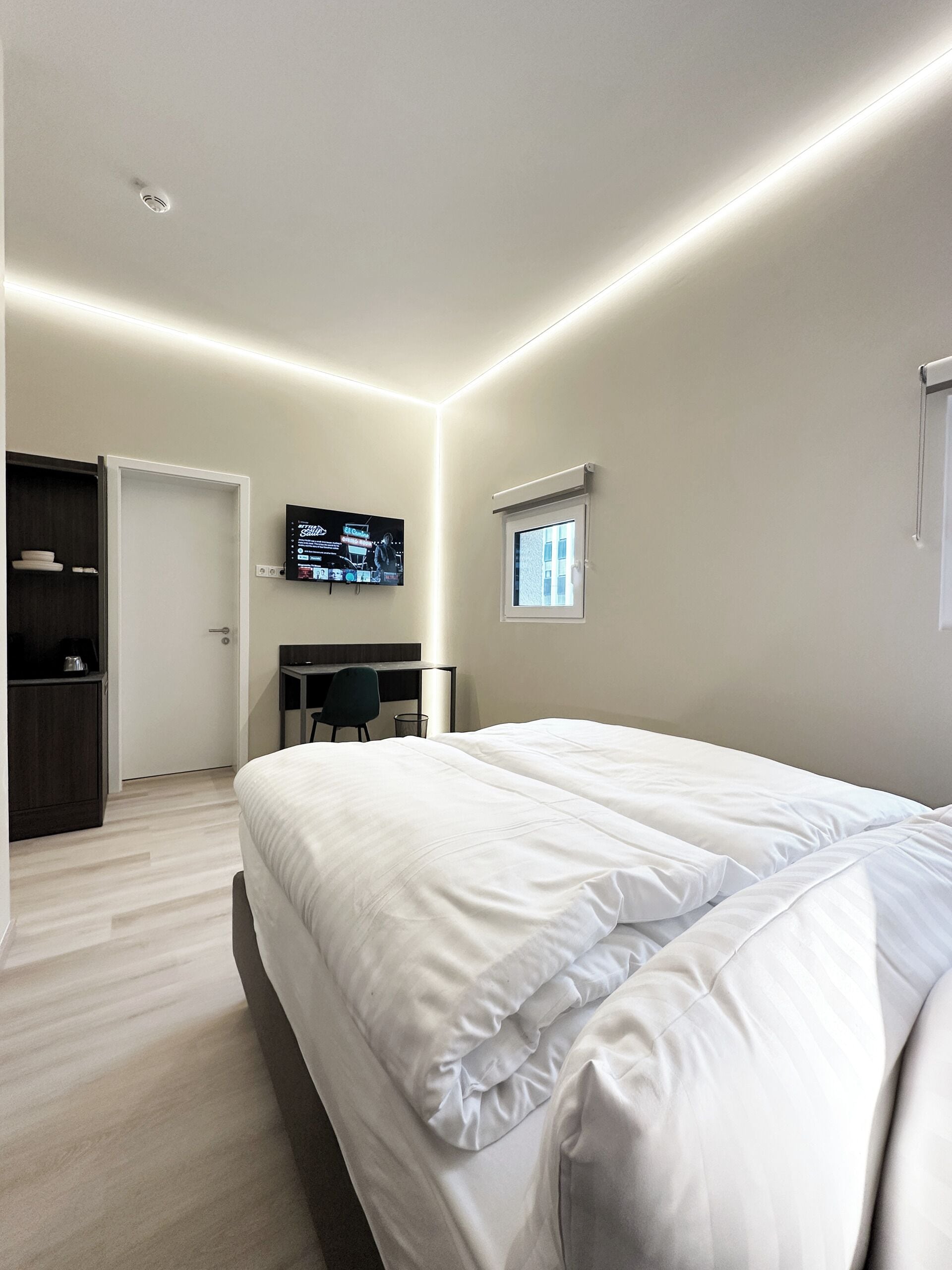 Ein modernes Hotelzimmer mit einem großen Bett, einem Schreibtisch mit Stuhl, einem Fernseher und einem kleinen Fenster.