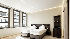 A modern bedroom with two beds, a nightstand, a wardrobe, and a large window. - Treasury Hotel (Neuss)