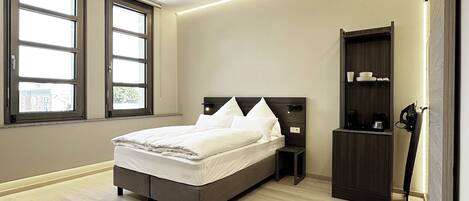 A modern bedroom with a large bed, built-in nightstands, a dark wooden wardrobe, and a large window providing natural light.