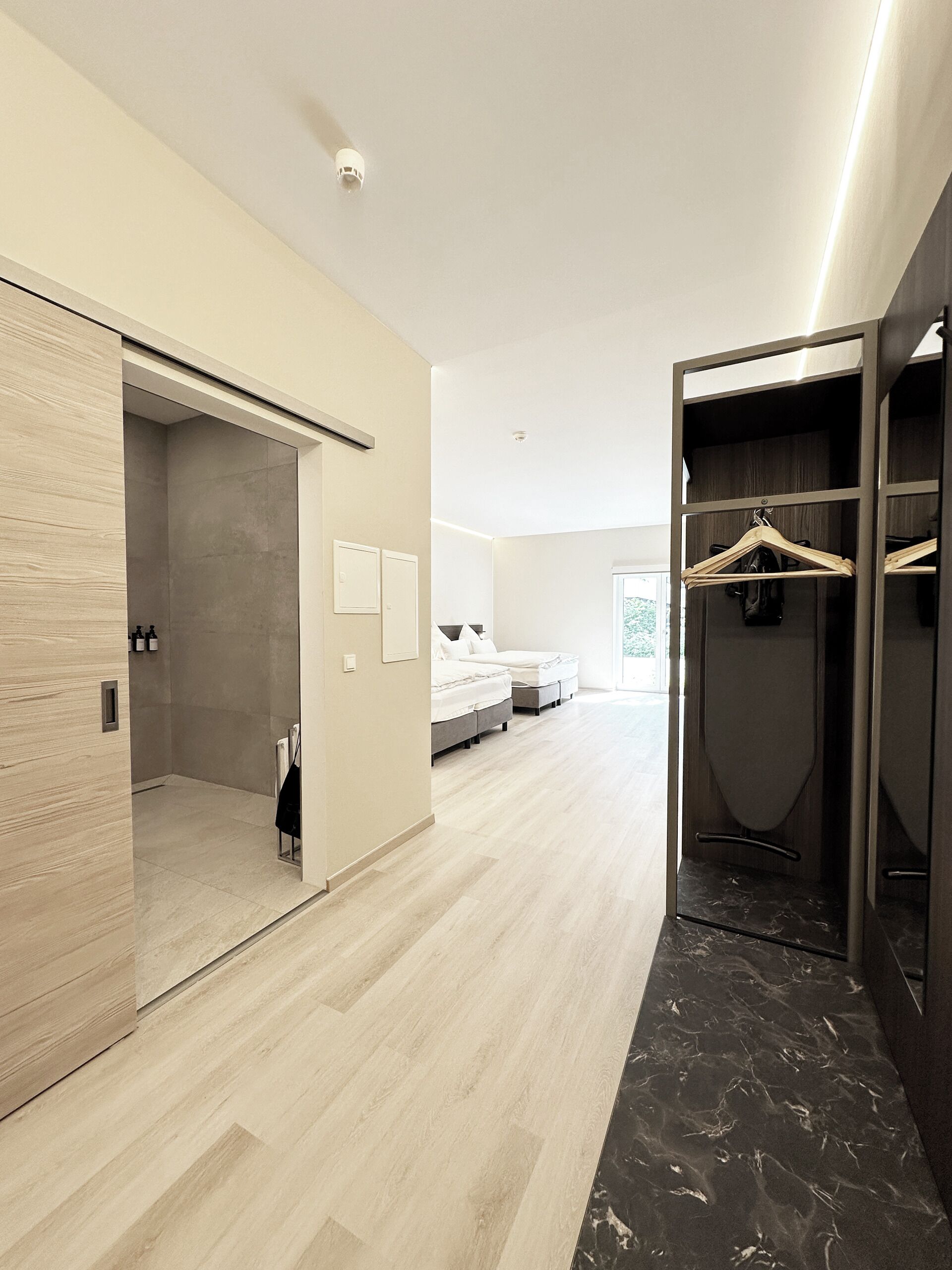 A modern bedroom with a wooden floor, a walk-in closet, and a bed with a white headboard.