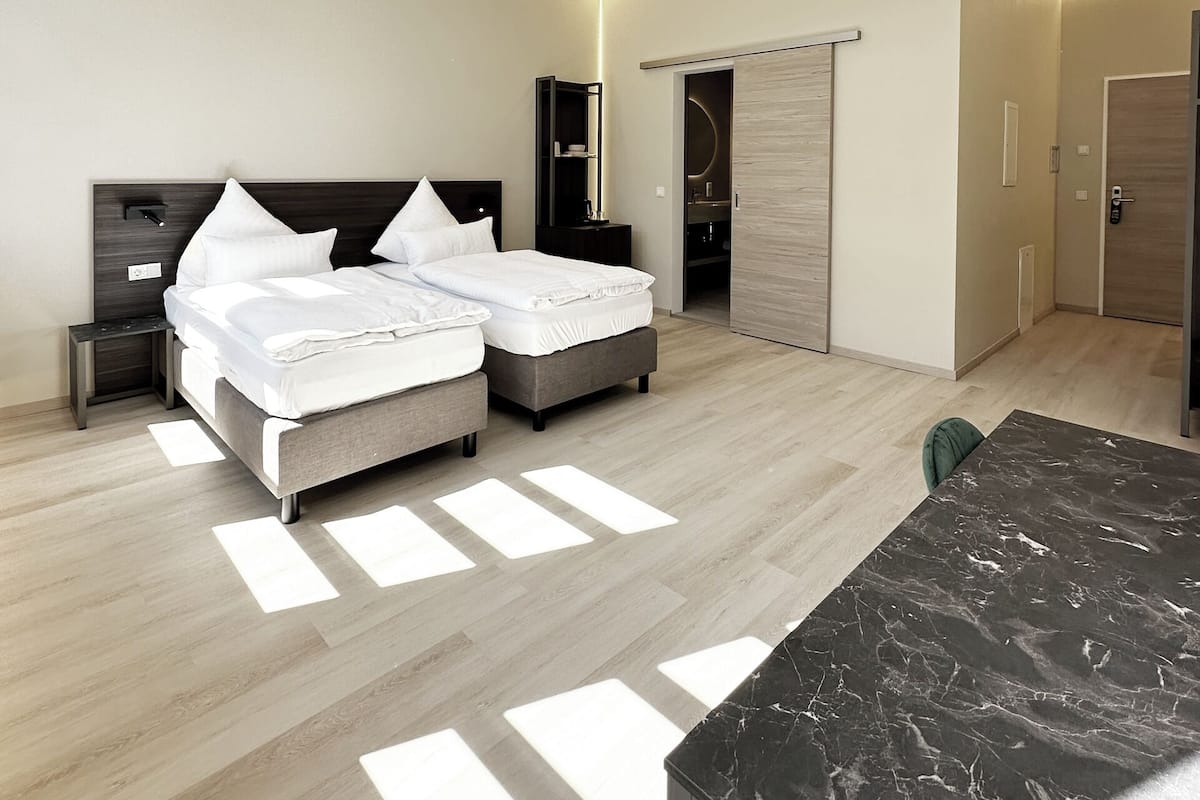 A modern hotel room with a bed, bedside tables, a desk, and a wardrobe.