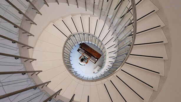 A spiral staircase with a piano in the center. - Treasury Hotel (Neuss)