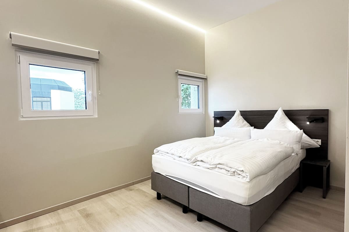 A bedroom with a bed, two windows, a nightstand, and a ceiling light.