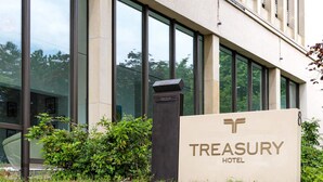 A sign for the Treasury Hotel with a modern building facade and large windows. - Treasury Hotel (Neuss)