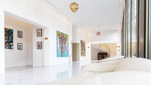 A modern hotel lobby with a white floor, art on the walls, a sofa, and a staircase in the background. - Treasury Hotel (Neuss)