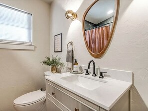 Bathroom features a white vanity, large mirror, and potted plant, with a window offering a view.
