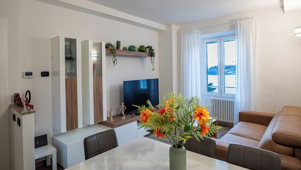 A modern living room with a TV, sofa, dining table, and a view of the outdoors. - BELLAVISTA APARTMENT (Blevio)