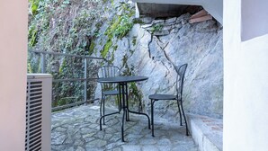 A stone patio with a table and chairs, a metal railing, and a stone wall with vegetation. - BELLAVISTA APARTMENT (Blevio)