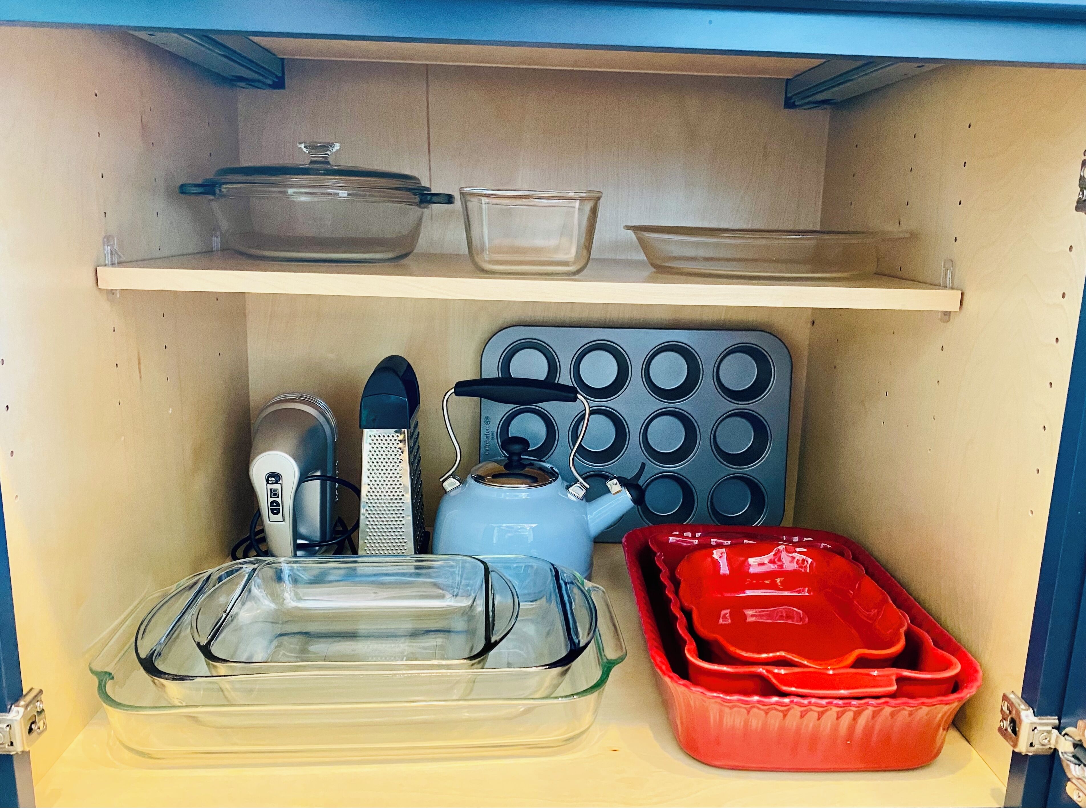 Une étagère de cuisine contenant divers ustensiles, notamment une bouilloire, une râpe, un moule à muffins et deux récipients en verre.