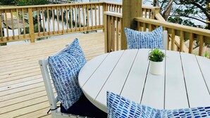 Een houten terras met een ronde tafel en stoelen, een leuning en uitzicht op huizen aan de overkant van het water.