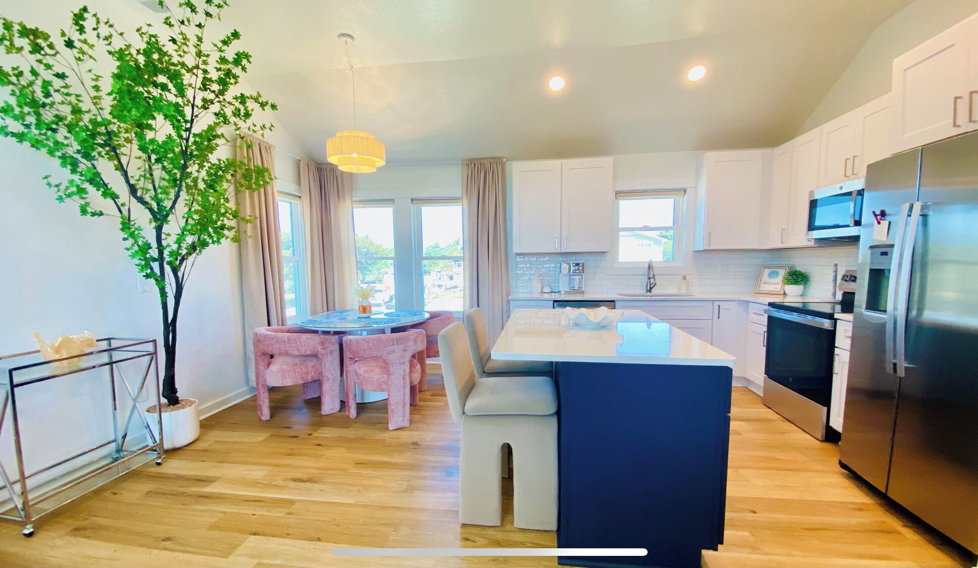A modern kitchen with white cabinets, a stainless steel refrigerator, and a dining area with a round table and chairs.
