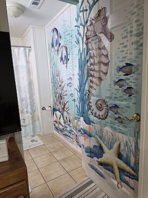 Un couloir orné d’une fresque représentant un paysage marin, avec un téléviseur et un banc en bois.