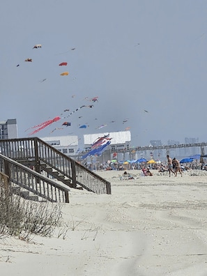Une plage avec une promenade en bois et un pont, une plage de sable, et une foule de personnes.