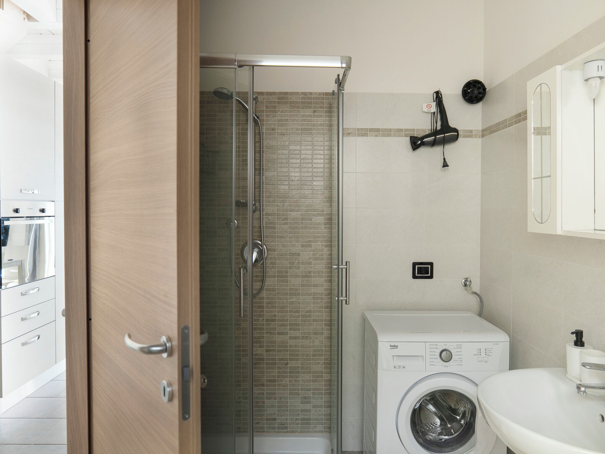 A modern bathroom with a glass-enclosed shower, a built-in washing machine, and a sink.