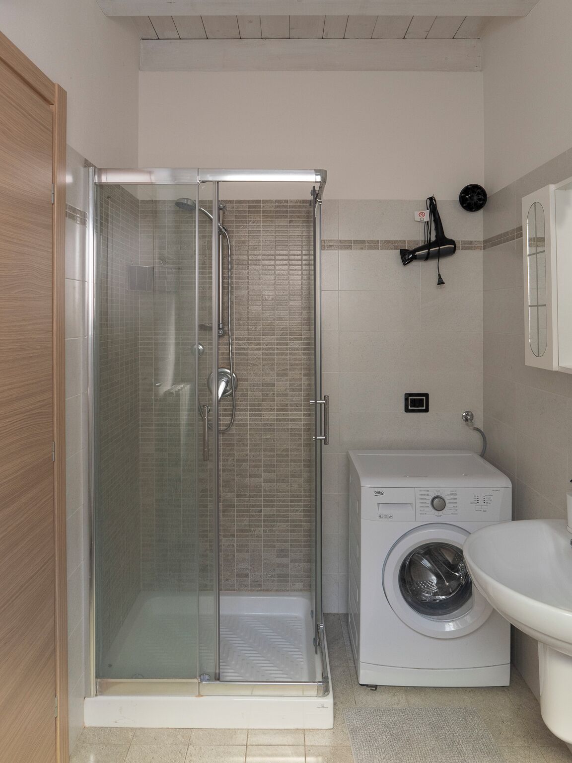 A bathroom with a glass-enclosed shower, a washing machine, and a sink.