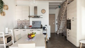 Eine moderne Küche mit weißen Schränken, einem Esstisch mit Stühlen, einer Obstschale und einer Treppe, die zu einer anderen Ebene führt.