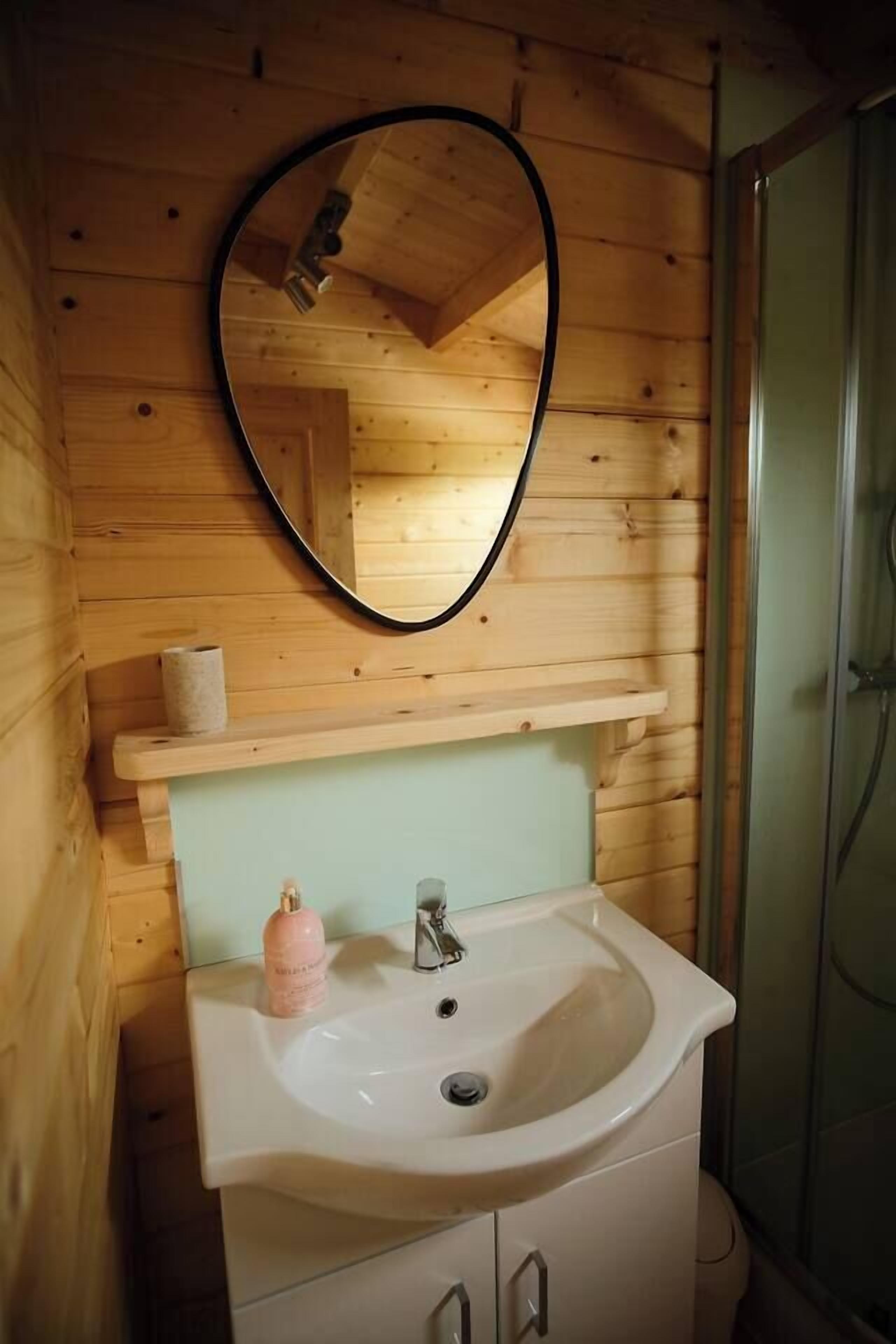 A wooden cabin bathroom with a white sink, a mirror, and a shower.