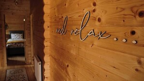Innenansicht einer Holzhütte mit einem Bett und einer Wand, auf der der Text "and relax" steht, verziert mit dekorativen Punkten.